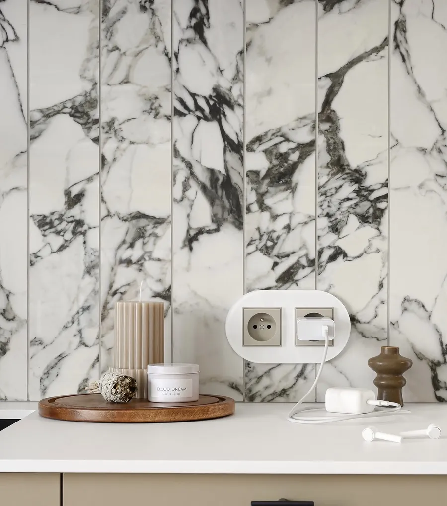 Karlik Icon taupe socket and switch with oval frame against Arabescato marble wall